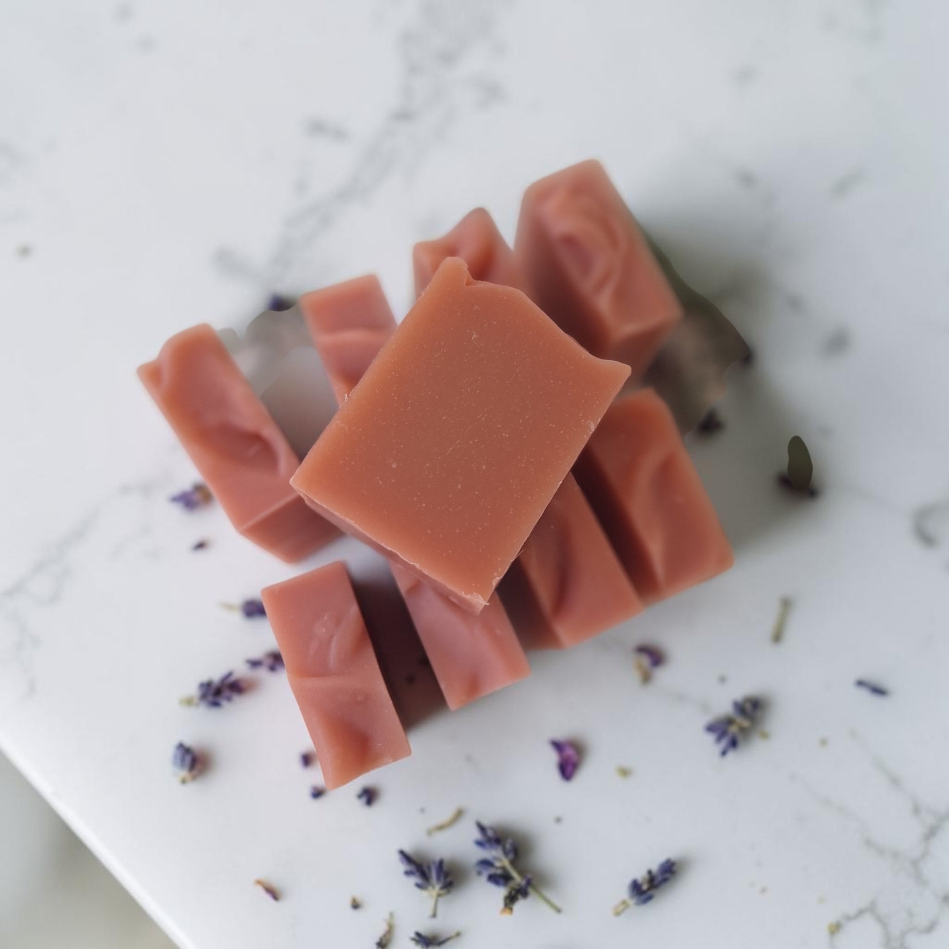 Several rectangular bars of dusty rose soap are arranged on a white marble surface with scattered dried lavender buds.