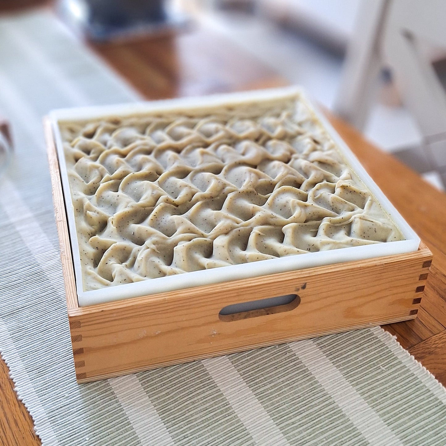 a square wooden slab of handmade soap on a wooden table with a natural green runner. Soap is green and textured