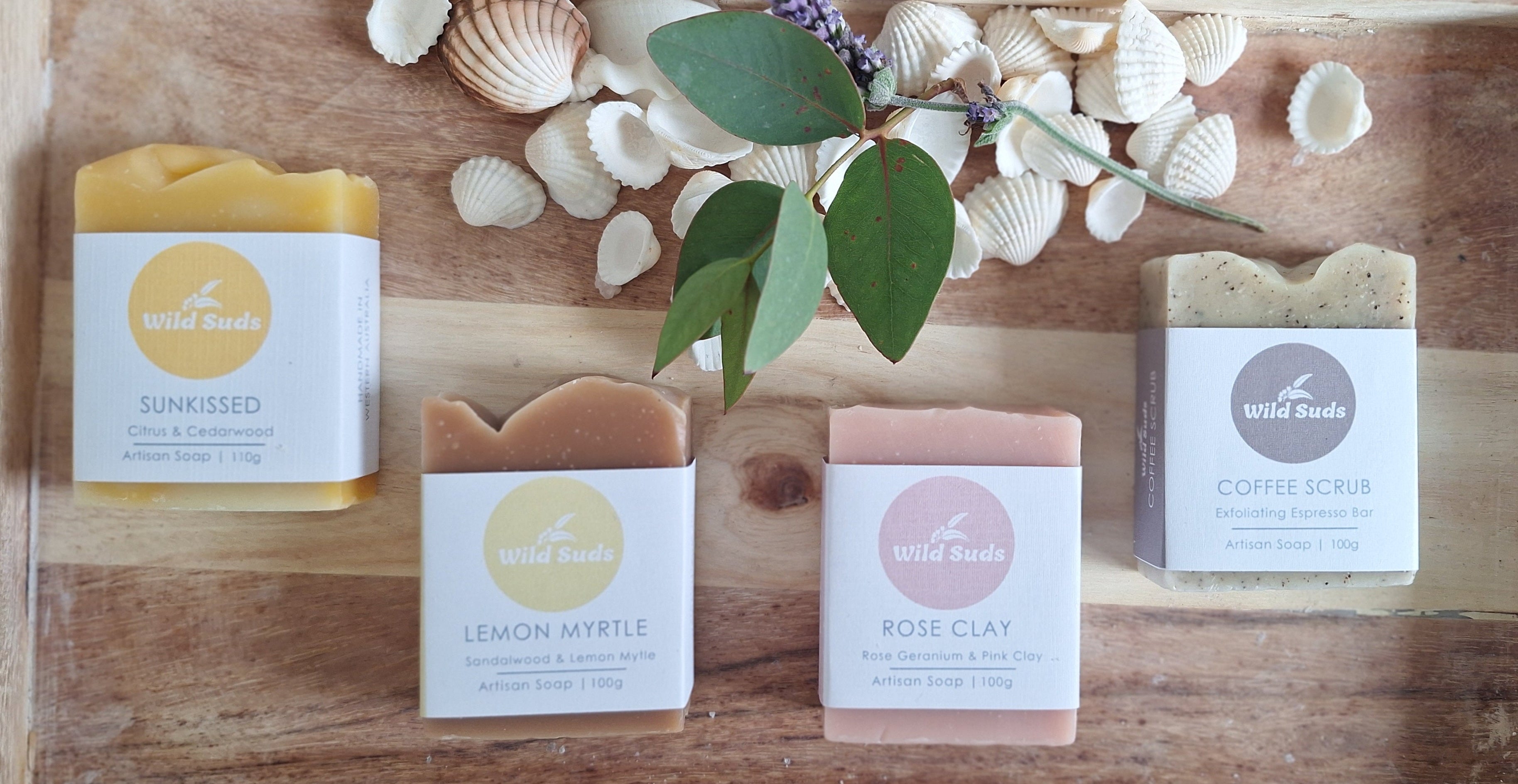 Collection of soap bars with labels on a wooden tray with seashells and leaves.
