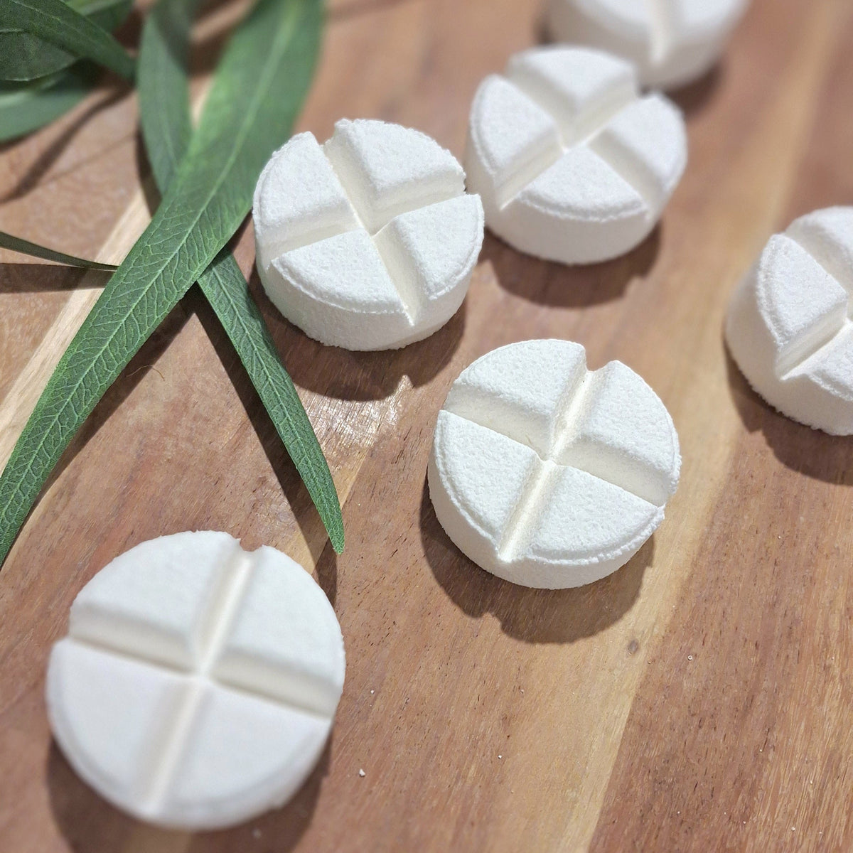 Several white round tablets with a cross-shaped cutout, arranged on a wooden surface with green leaves in the background.