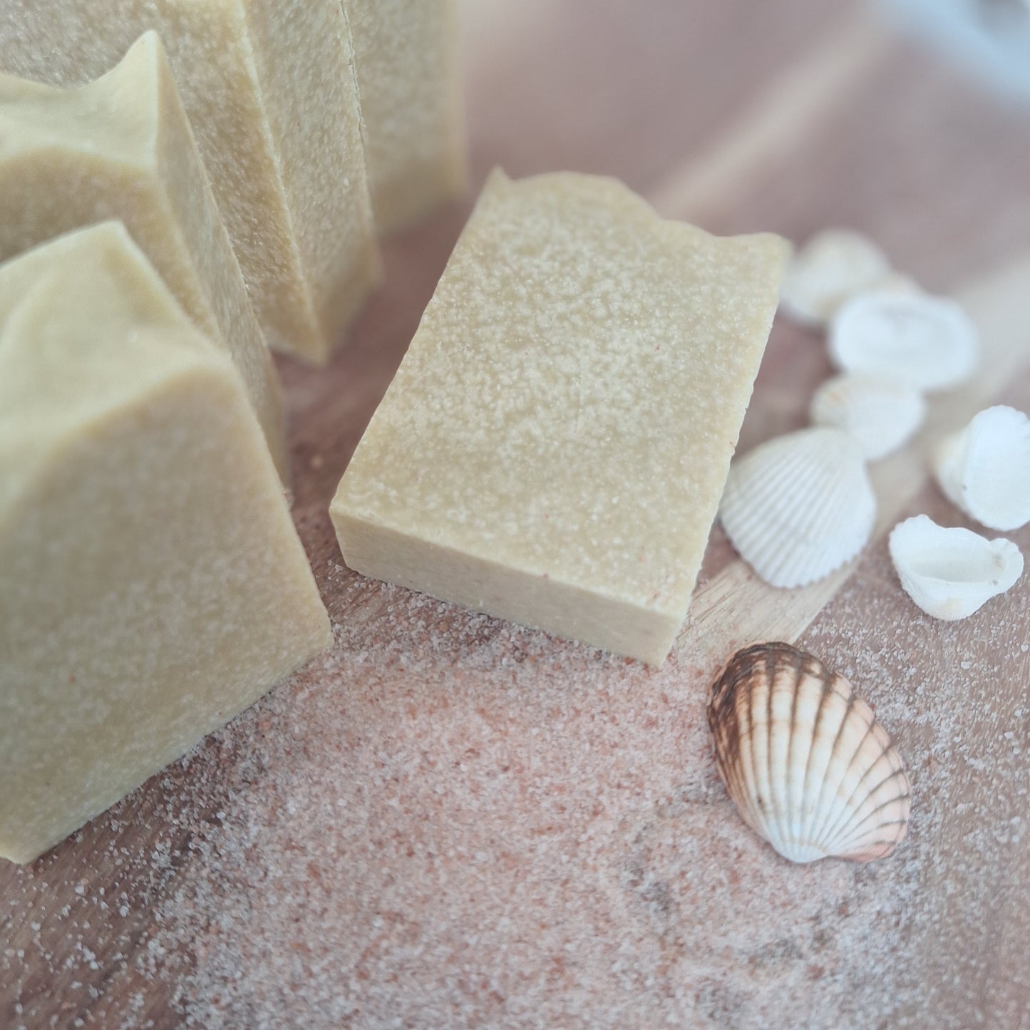 Several rectangular bars of pale beige soap arranged on a sandy surface with white seashells nearby. Himalayan salt surrounds the soap by Wild Suds made in Western Australia